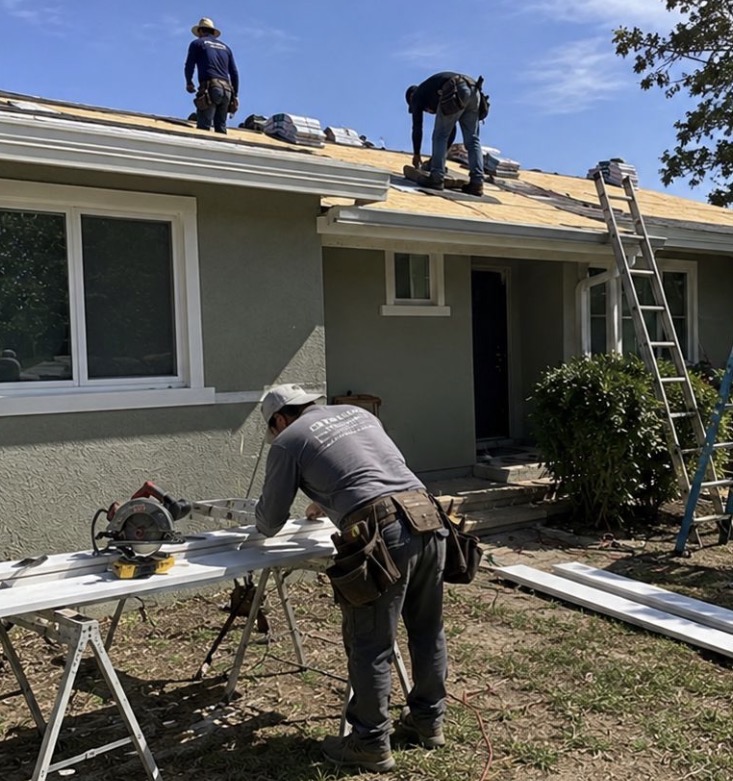 Roofers re-decking a roof while a fitter cuts trim below